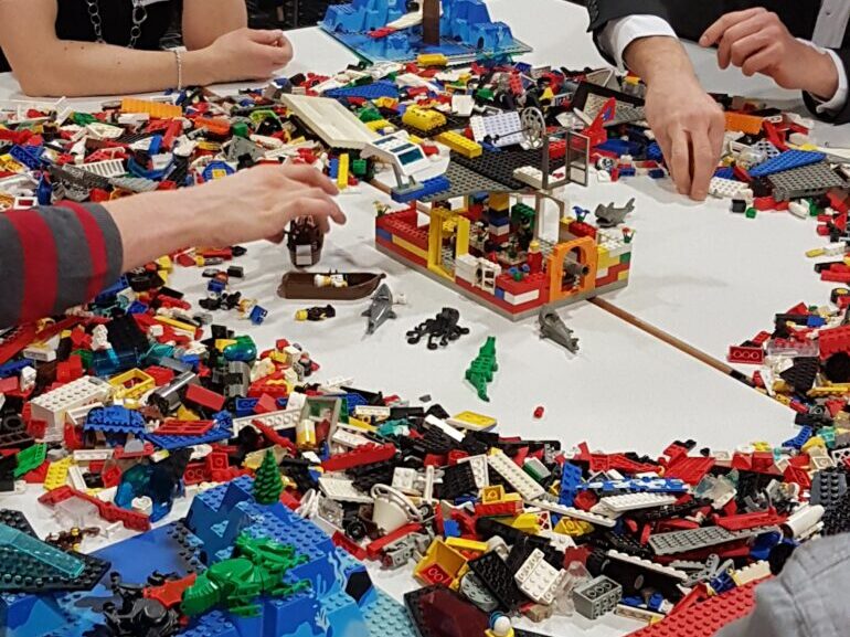 Tisch einer Arbeitsgruppe. Es liegen bunte Legosteine am Tisch. In der Mitte ist ein Legoobjekt zu sehen.